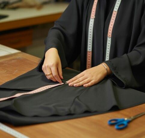 Professional abaya tailor hemming traditional black abaya with measuring tape and sewing tools